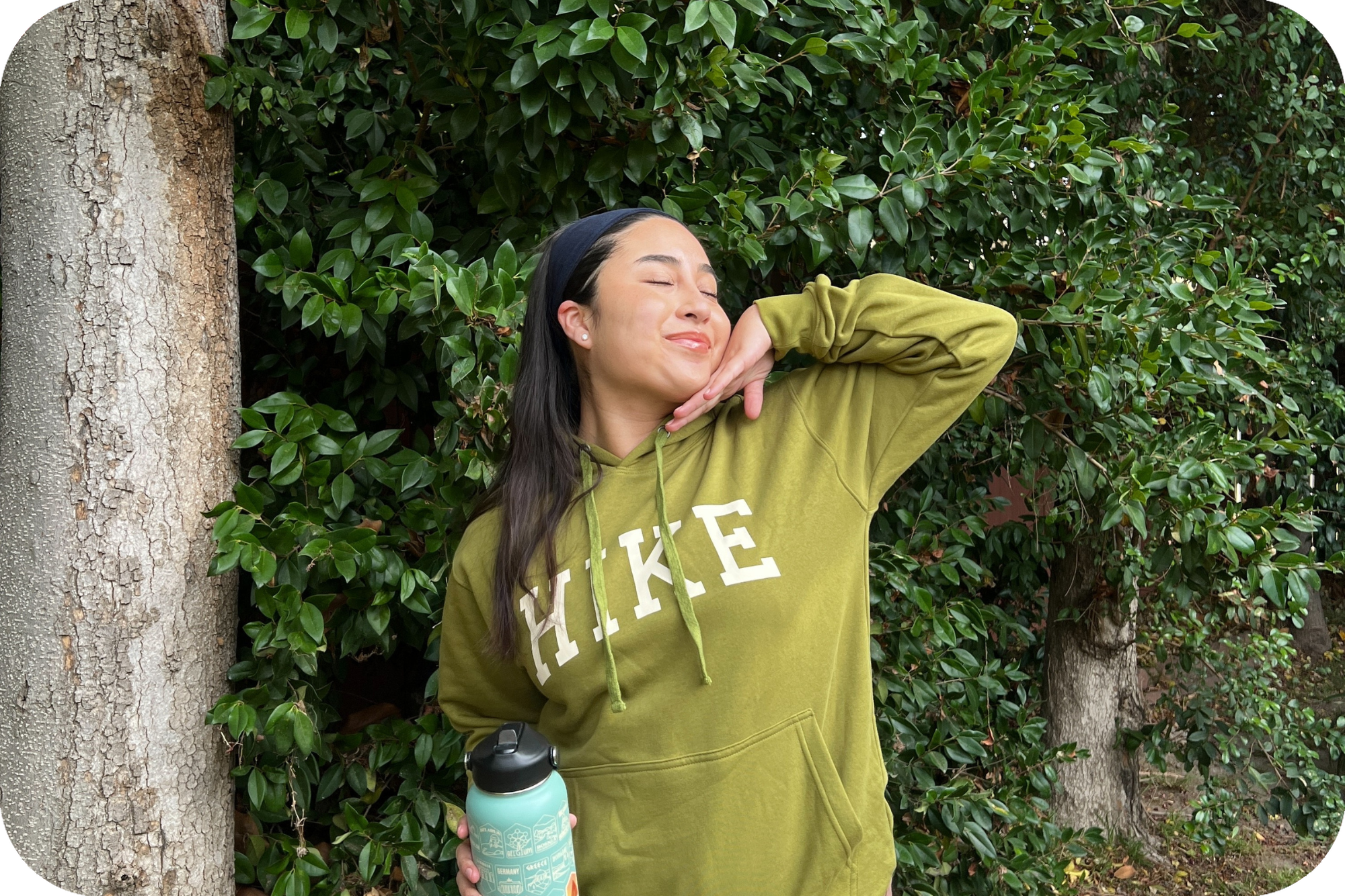 Woman wearing green hike hoodie posing outside with the bucket list travel water bottle