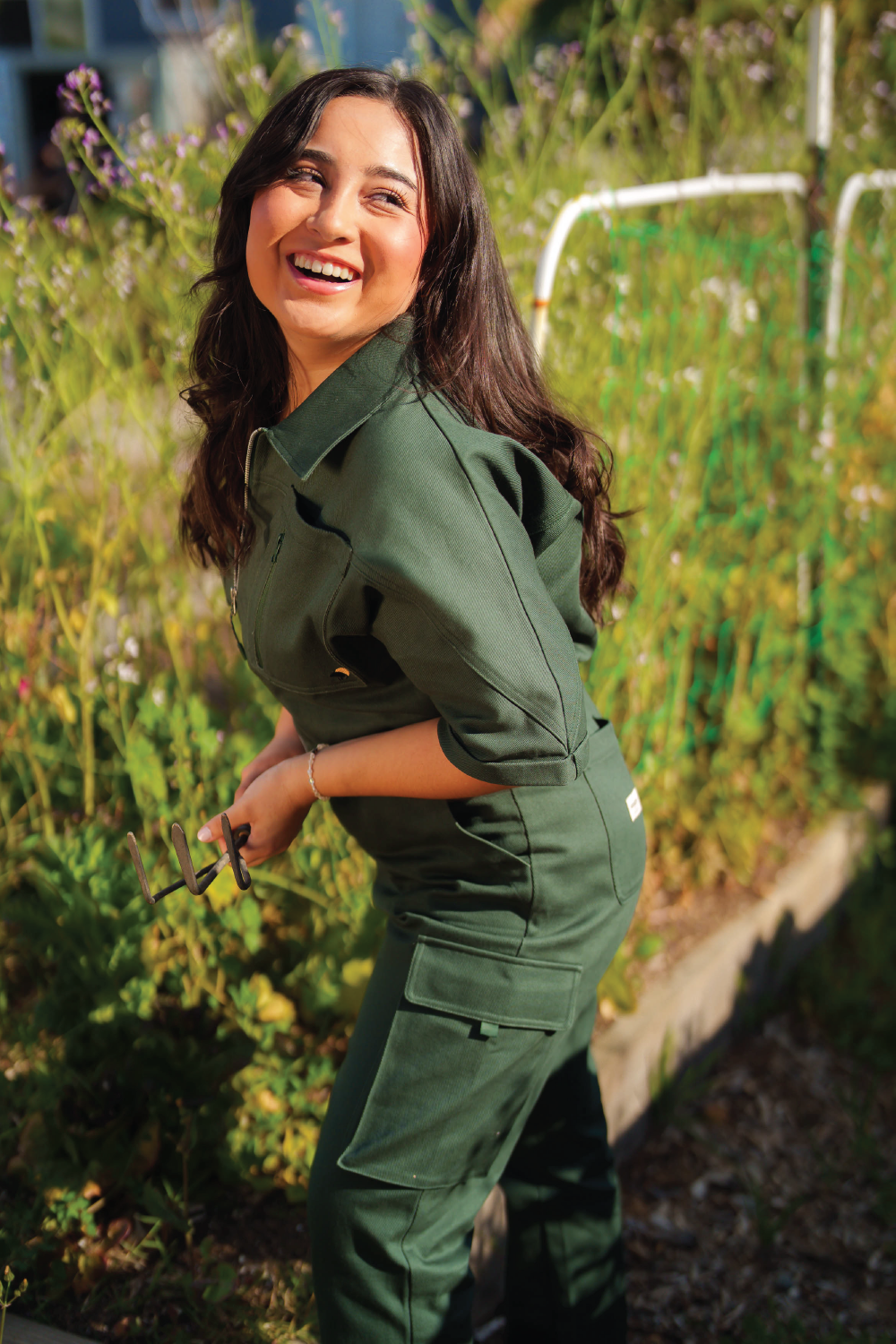 woman with brown hair wearing green denim jumpsuit in sunny garden in Los Angeles Biedermannsdorf