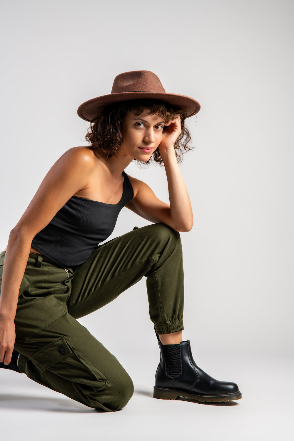 woman in army green cargo outdoor hiking camping pants and asymmetrical black top and wide brim hat #color_forest