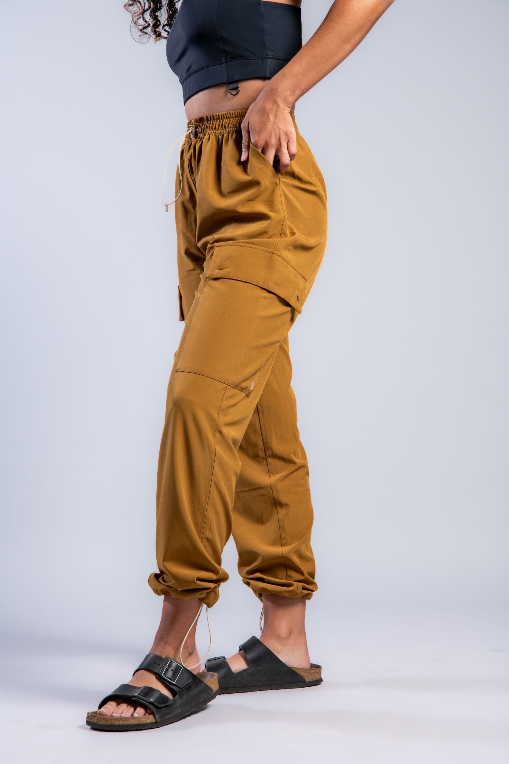 brown woman in black tank top and brown loose lounge pants and birkenstocks #color_ochre