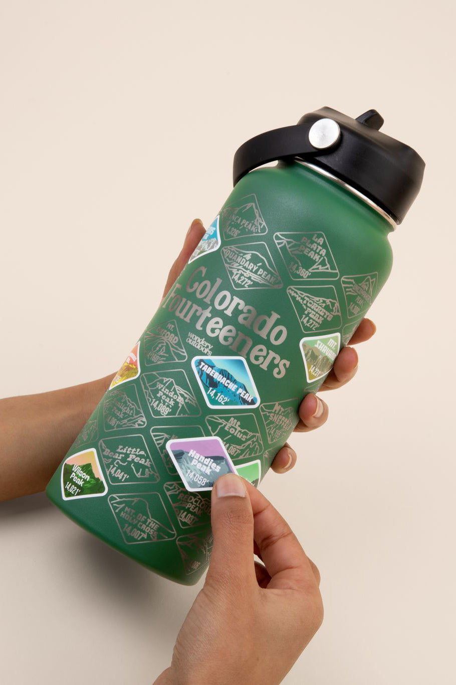 hand placing waterproof stickers on bottle green Colorado engraved travel bottle with strap