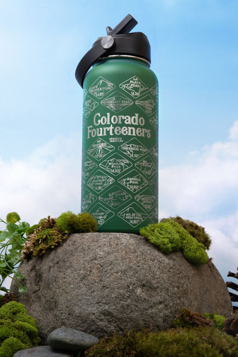 green Colorado engraved travel bottle with strap on top of rock with moss with a blue sky and white cloud background