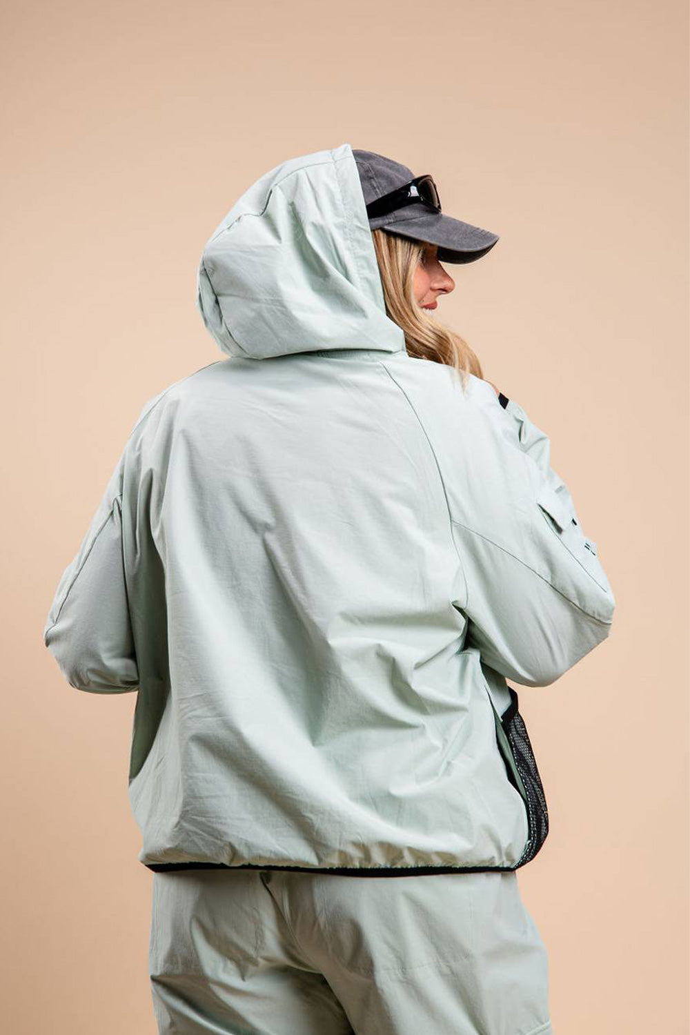blonde woman with lightweight windbreaker jacket hood on over hat and sunglasses