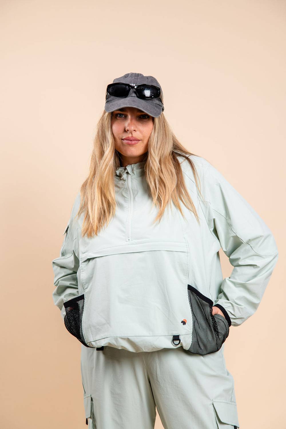 Blonde woman in mint green lightweight jacket with pockets and dad hat with sunglasses
