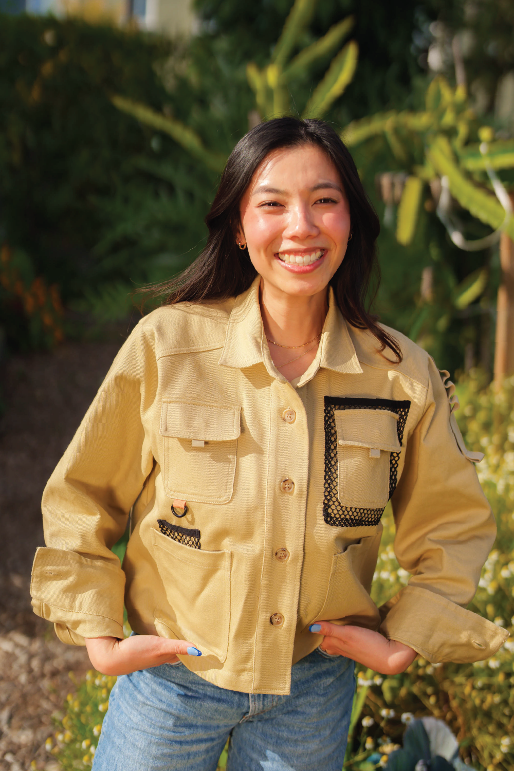 asian woman smiling while in khaki brown denim jacket with long sleeves and denim Levis jeans with garden in background
