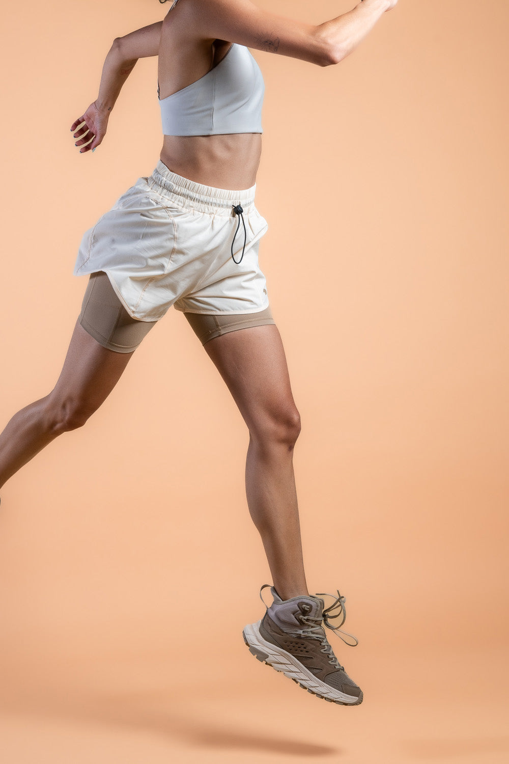 woman in cream lightweight running shorts and biker shorts with side pocket #color_cream/Sand