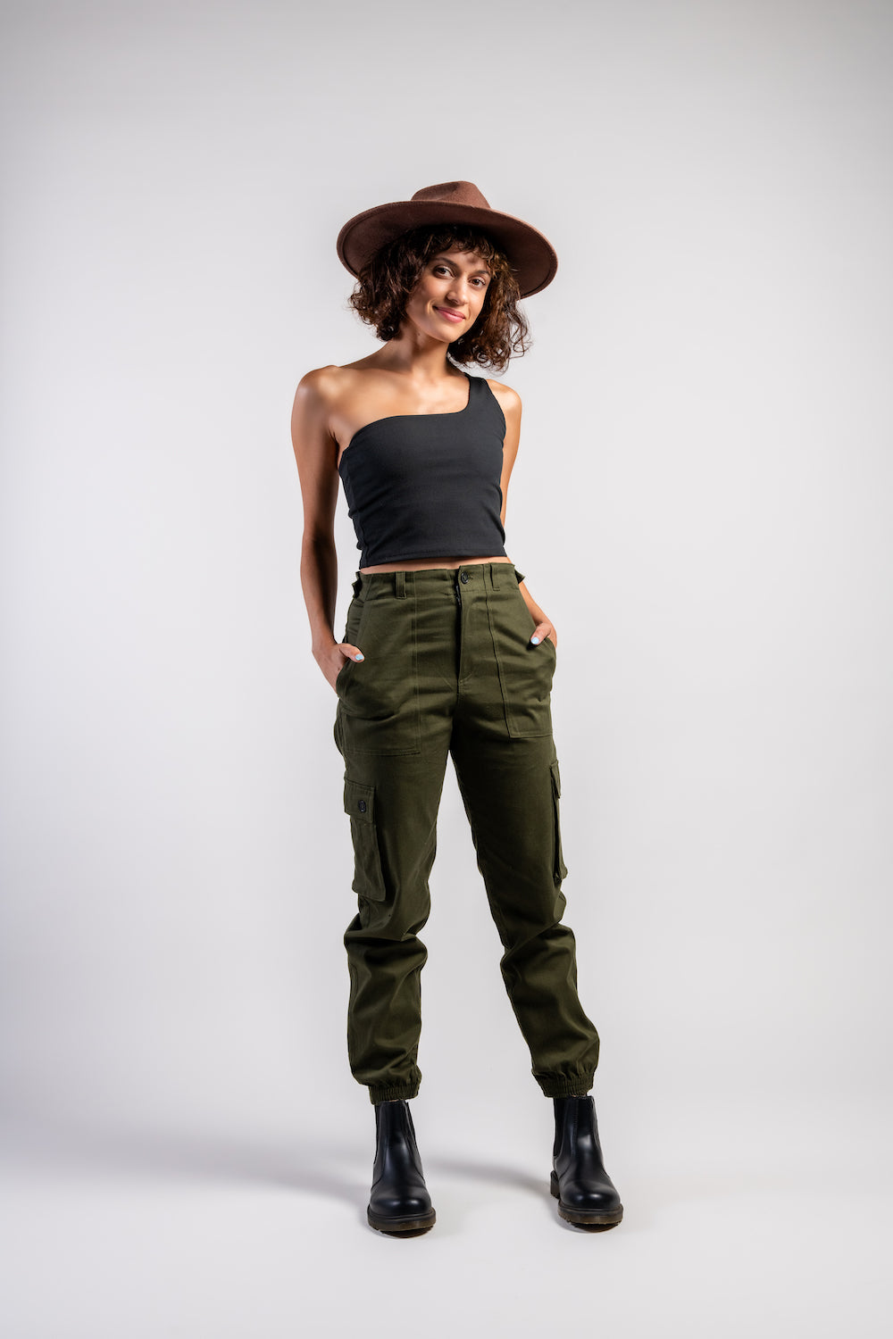 woman in army green cargo outdoor hiking camping pants and asymmetrical black top and brown hat #color_forest