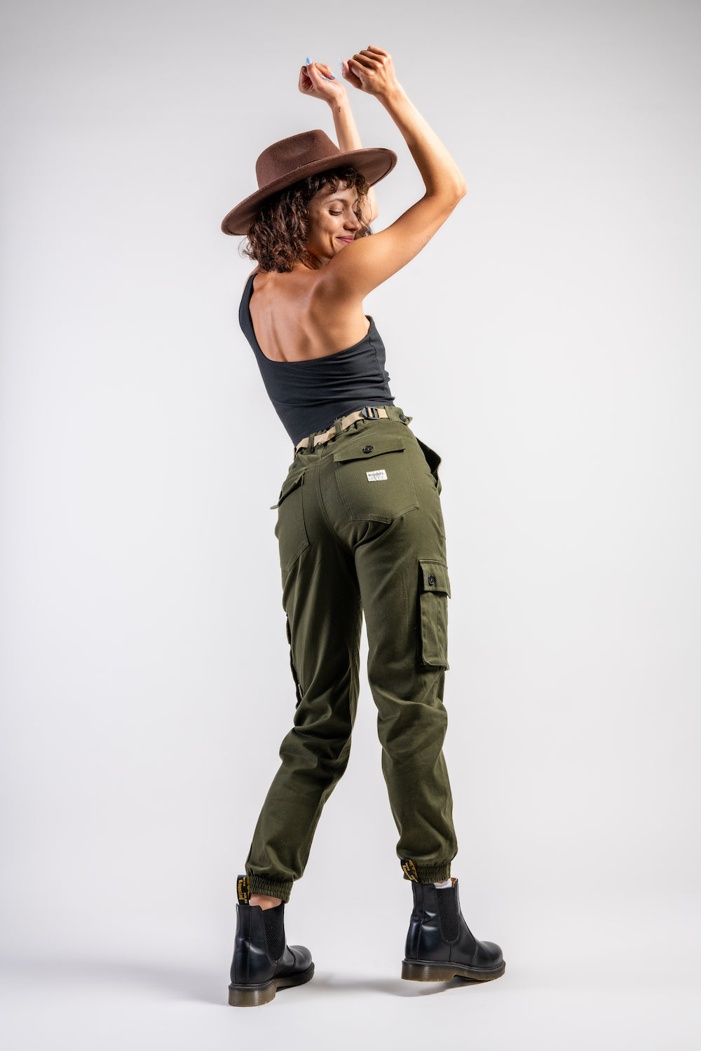 woman in army green cargo outdoor hiking camping pants and asymmetrical black top and wide brim hat #color_forest