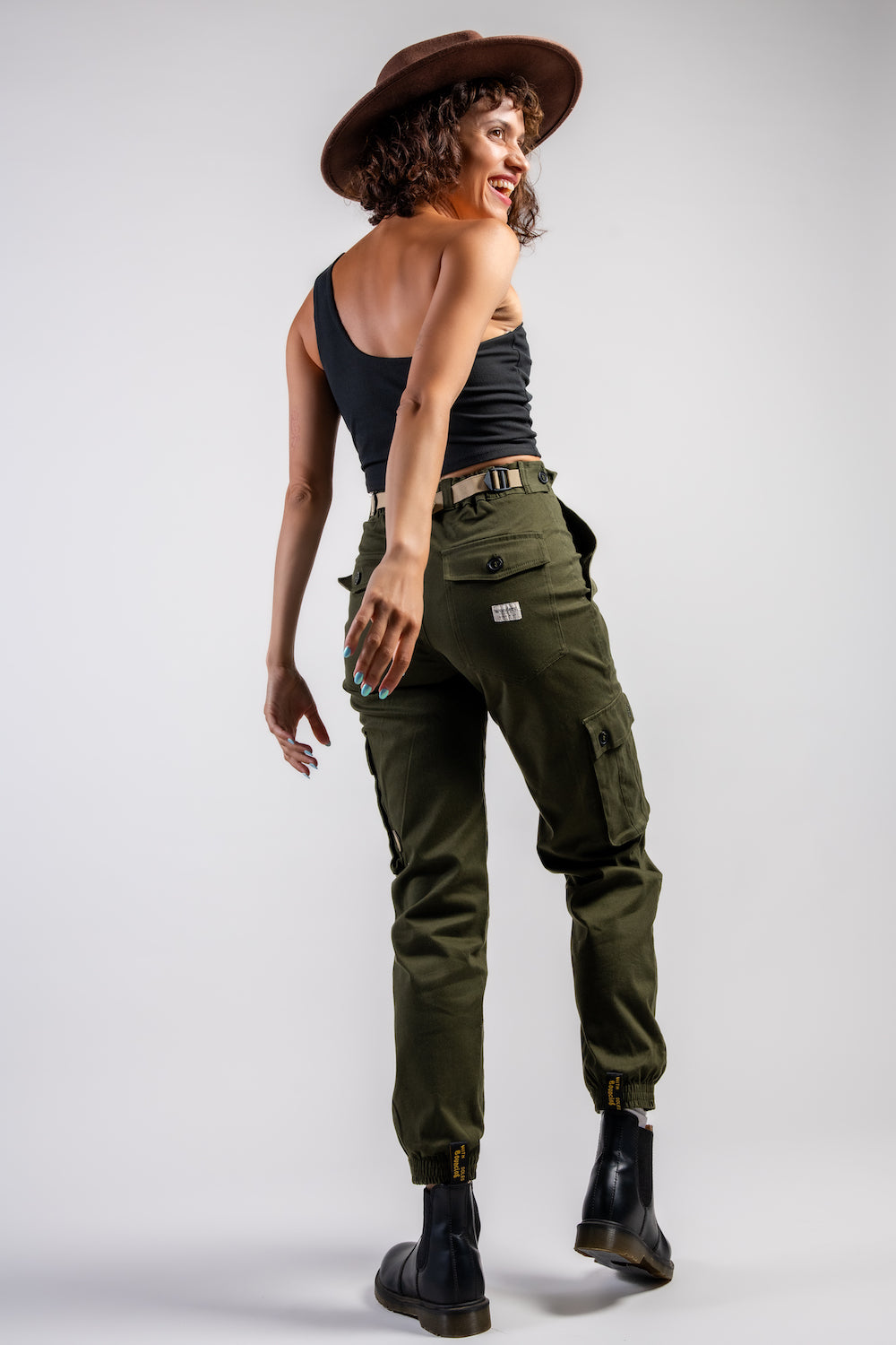 woman in army green cargo outdoor hiking camping pants and asymmetrical black top and wide brim hat #color_forest