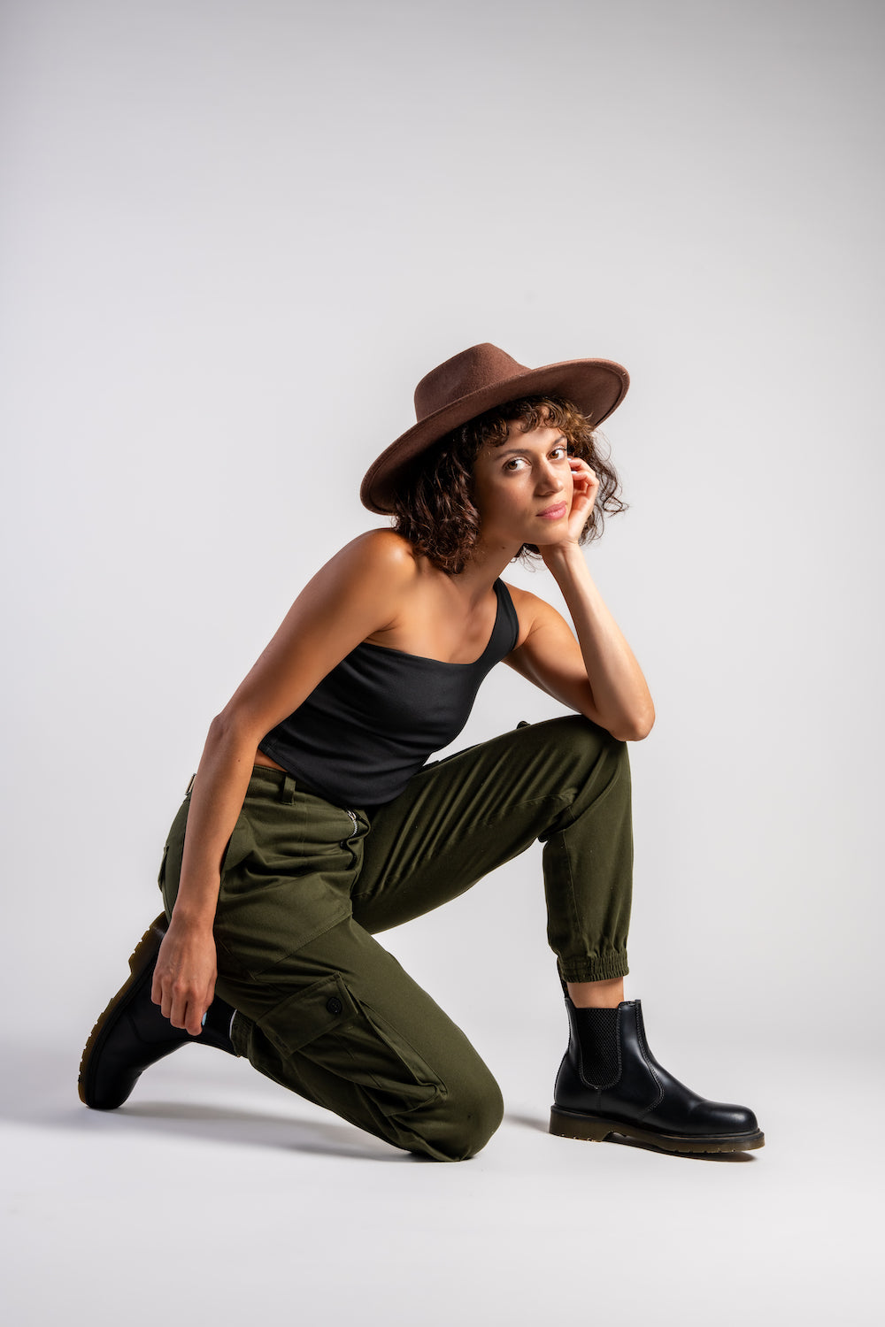 woman in army green cargo outdoor hiking camping pants and asymmetrical black top and brown hat #color_forest