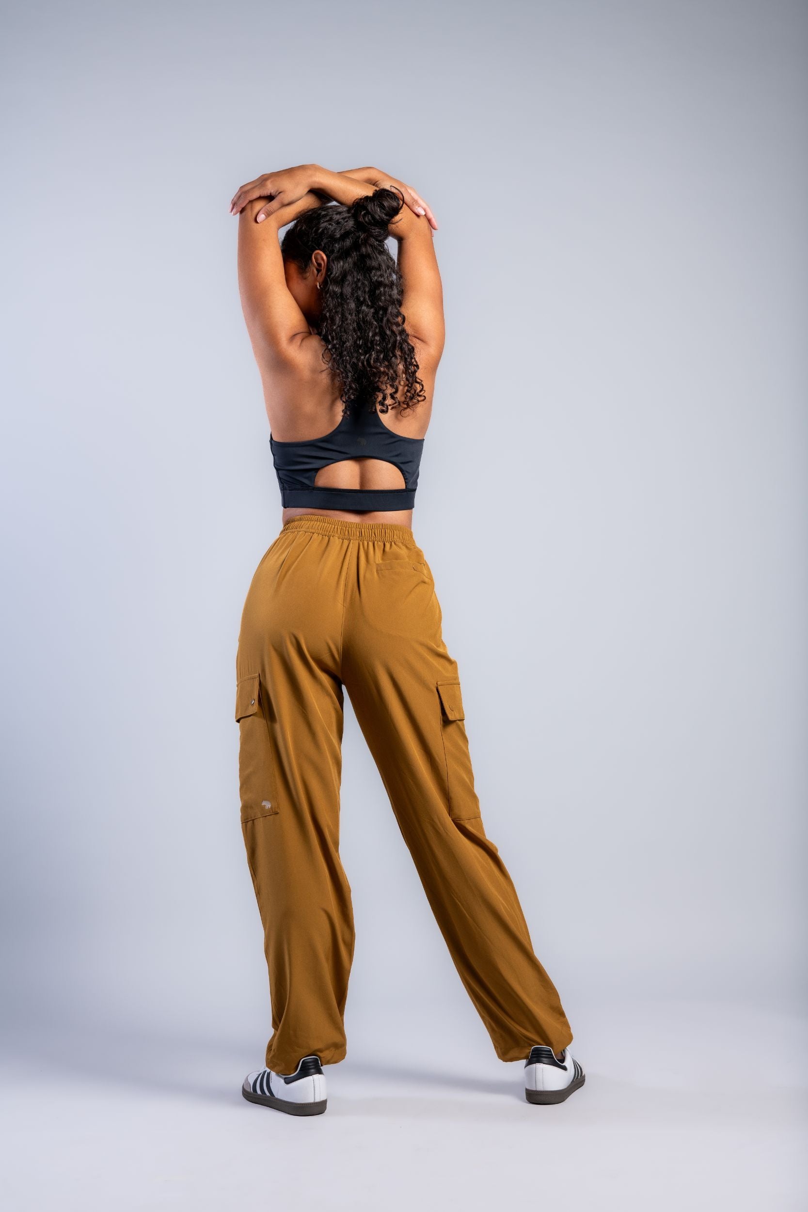 woman stretching in lounge cargo pants brown woman in black tank top and brown loose lounge pants and adidas #color_ochre